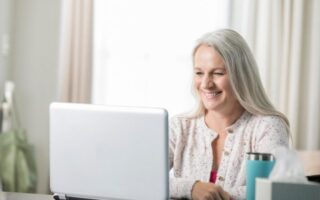 A white haired woman smiling at a laptop
